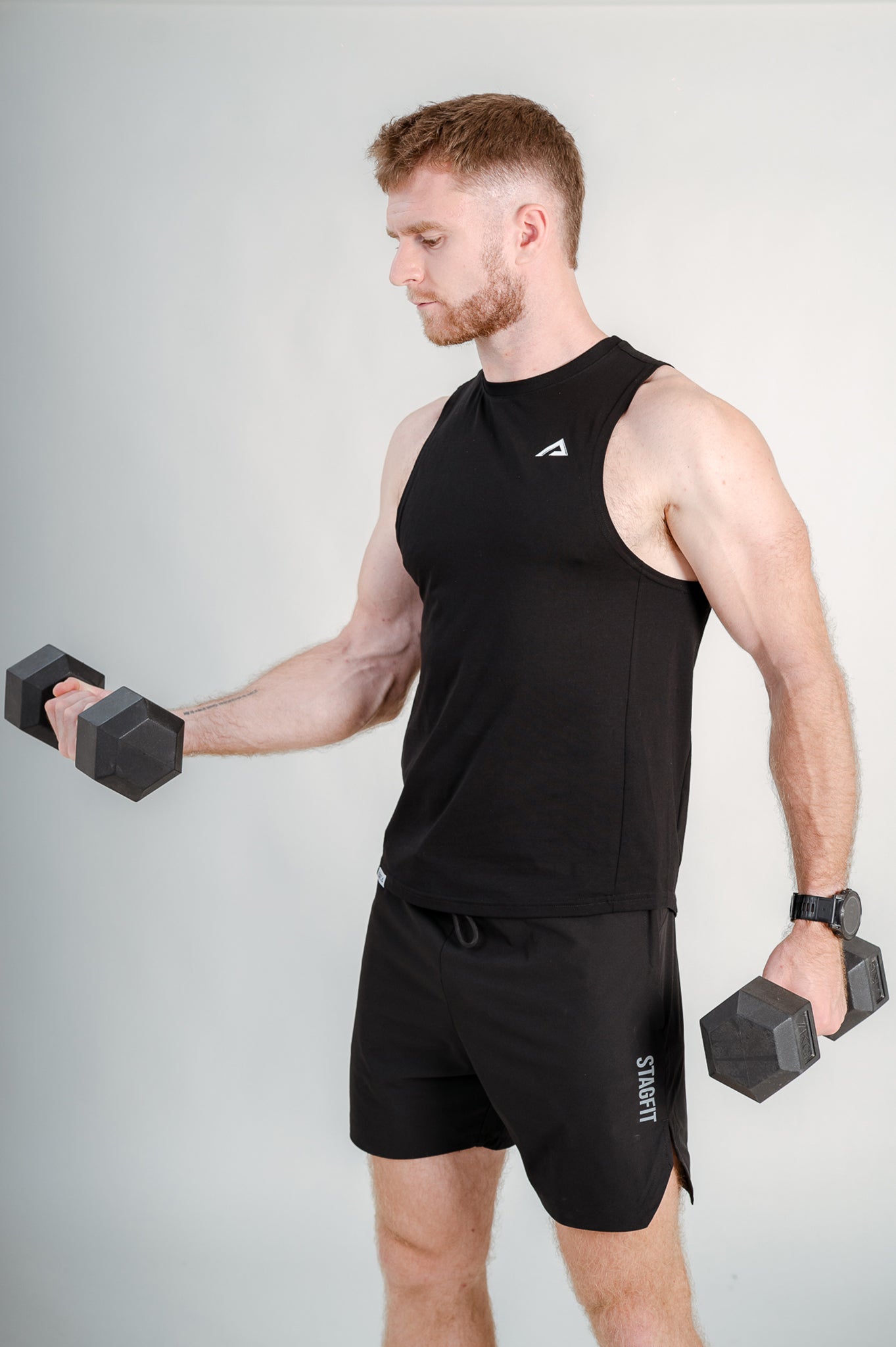 Athlete lifting dumbbells wearing StagFit black drop arm tank top.